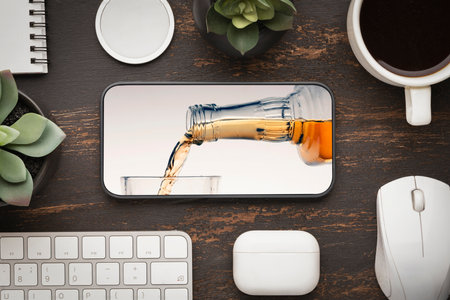 online order alcohol delivery or meeting with friends after work or going to a bar. a bottle of whiskey and a glass on the screen of a smartphone mobile phoneの写真素材