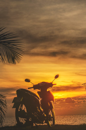 A motorbike on the background of an orange sunset by the sea. A serene holiday in Thailand, relaxation. Tourism and vacation travel in Asiaの写真素材