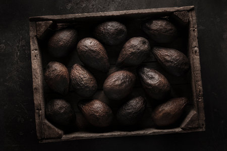 Old blackened brown avocados in an old wooden box - Beautiful dark black textured background, top...
