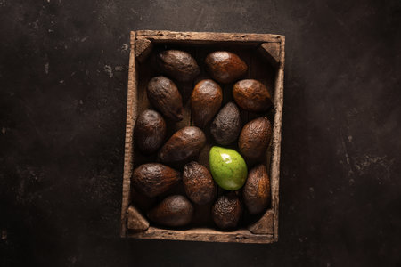 Loneliness in the crowd. One green avocado in a box with old brown avocados. Texture background top view flat layの写真素材