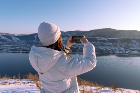 Photographing nature on a winter adventure trip - A girl in a white jacket takes pictures of a...
