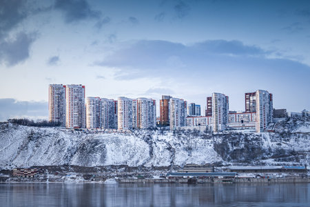 Beautiful view of a residential neighborhood of apartment buildings on a winter evening on the banks of the Yenisei River in Krasnoyarsk, Russia. Spectacular Modern HighRise Buildings Situated on a Snowy Cliff with an Incredible River Viewの写真素材