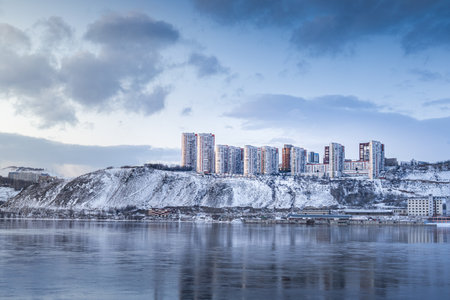 Beautiful view of a residential neighborhood of apartment buildings on a winter evening on the banks of the Yenisei River in Krasnoyarsk, Russia. A SnowCovered Urban Landscape Featuring Modern Buildings Situated near Waterの写真素材