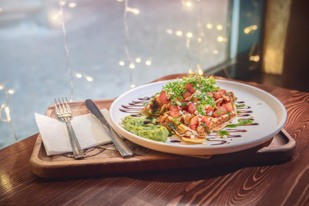 Waffle with tomatoes, avocado, mozzarella and pesto on the table in the coffee shop by the window....
