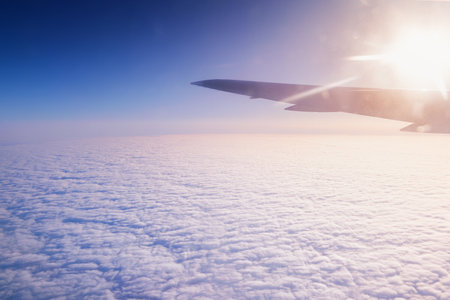 This aerial perspective shows beautiful clouds beneath an airplane wing, glowing vividly in the...