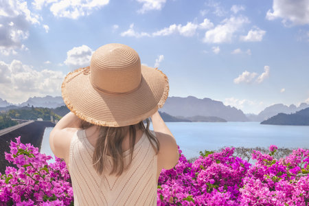 Woman tourist traveler in a wide-brimmed hat takes pictures of Lake Checo Lan and Dam from viewing point, rear view. Thai Tourist Spots such as Rachaphrapha Dam in Khao Sok Park in Phang Nga Provinceの写真素材
