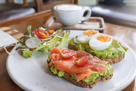 Delicious toasts with avocado, smoked salmon, eggs and a variety of fresh vegetables are served on a...