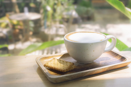 Breakfast in the morning outdoors - A cup of warm cappuccino coffee in a white clay mug with cookies on a wooden tray in a lush setting.の写真素材