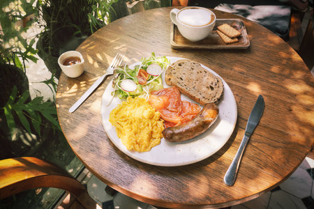 Scrambled eggs, fried pork sausage and sliced smoked salmon slices with rye bread toast and salad with radishes and Coffee with biscuits. A fresh breakfast in the sunshine outside.の写真素材