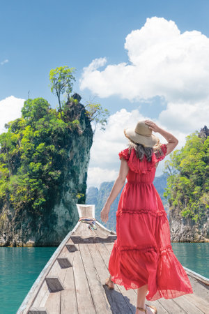 A woman elegantly dressed in a stunning red dress poses majestically against a gorgeous tropical...