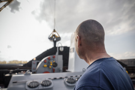 At the port, a worker oversees the process of loading coal onto a barge with the aid of a large...