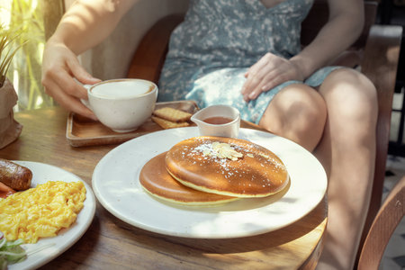 Delicious pancakes served with coffee and syrup in a cozy cafe setting. A woman in the background...