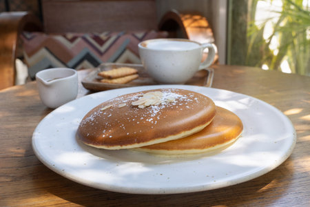 Tasty fluffy pancakes served with coffee and biscuits at a cozy cafe in the morning sunlight. Sweet...