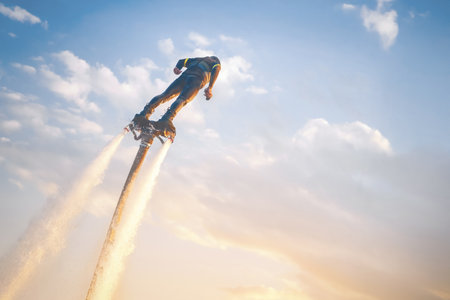 A flyboard athlete hovers over the water against the sunset sky, propelled by powerful jet streams...