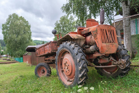 Vintage red old tractor t16 parked in a lush green field near a rustic farmhouse on a cloudy day in the countrysideの写真素材