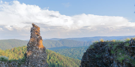 A unique rock formation stands tall amidst lush green forests, revealing the vastness of the mountainous terrain.の写真素材