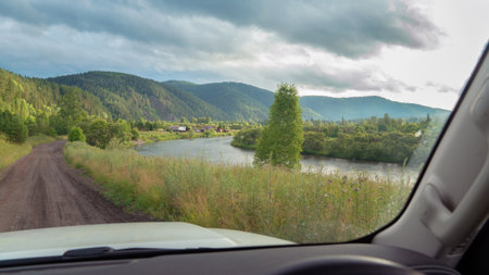 Scenic drive along riverside landscape with mountains in background during cloudy afternoon. Road trip to remote villages in Siberia and Russia river viewの写真素材