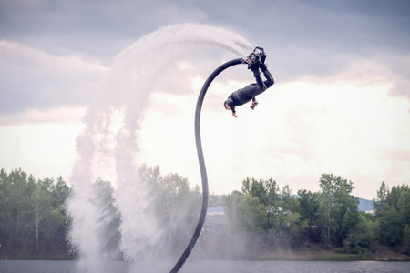 Flyboarding session showcases thrilling acrobatics over the water at a scenic lake on a cloudy...