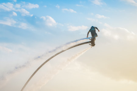 Flyboarding adventure in clear skies over the ocean during sunset with a rider soaring high. Flyboarding athlete with jet stream flying on a flyboard against the sky extreme sportsの写真素材