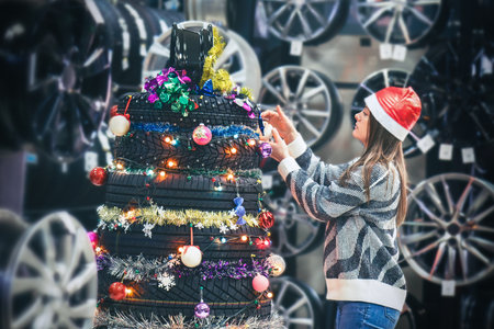 Woman decorates a tire Christmas tree in festive clothing, embracing holiday spirit with creativityの写真素材