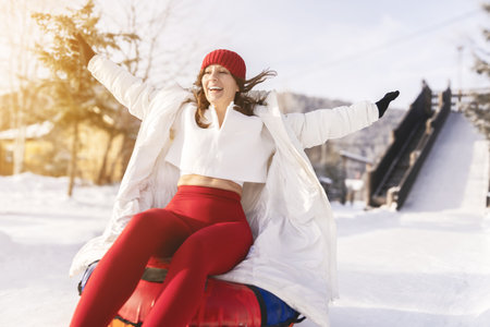 young woman with a bright smile enjoys the thrill of sliding down a snow-covered slope on an...