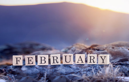 February is a close-up word made of wooden cubes in nature, against the background of blue mountains. February is the last month of winter.の写真素材