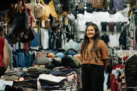 Khao Lak, Thailand, 24 11 2025: Small business in Thailand - a female salesperson smiles and waits for tourist customers, standing in her clothing store at the night market. High quality photoのeditorial素材