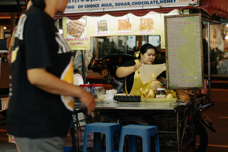 Khao Lak, Thailand, 24 11 2025: Small business street photo - Thai woman prepares traditional Thai Asian flatbreads, Roti pancakes from a street cart or kiosk on Kaolak night street. Local business isのeditorial素材