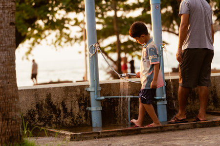 Khao Lak, Thailand, 24 11 2025: A boy washes his feet after swimming in the sea and playing on the beach, Dad is standing next to him. The atmosphere of a holiday in Thailand by the sea, street photosのeditorial素材