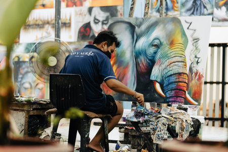 Khao Lak, Thailand, 24 11 2025: A small business in Thailand is a street artist working on a painting of an elephant. The artist sits on a chair and paints a picture with acrylic or oil paints. Highのeditorial素材