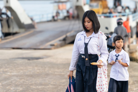 Koh Kho Khao Island, Thailand, 05 30 2026: Two schoolgirls are walking home after school on Koh Kho Khao Island in Thailand. They wear white uniforms and are arriving from a ferry ride, carrying bagsのeditorial素材