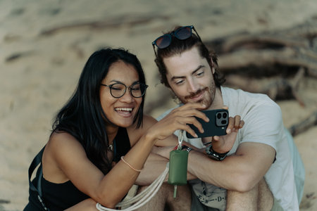 Khao Lak, Thailand, 16 11 2025: A young couple in love looks at their photos that they took sitting on the beach in the evening. A Thai woman and a European man enjoy a vacation by the seaのeditorial素材