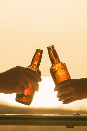 Two bottles of beer on the background of the setting sun in the hands of a couple in love or friends...