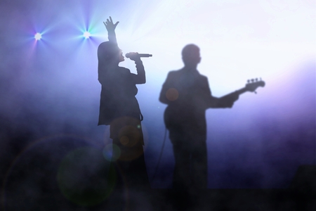 Women on stage singing with guitarist under spotlightの写真素材