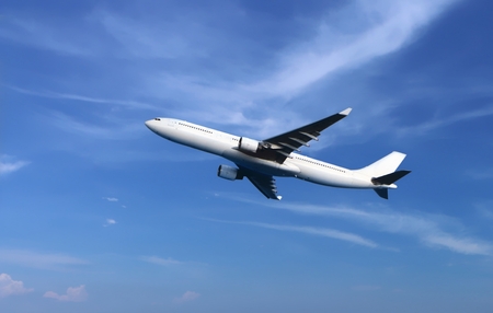 Passenger airplane flying under cloudy blue skyの写真素材
