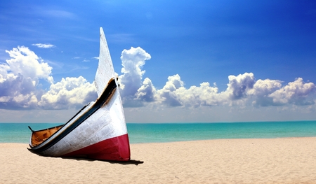 Small wooden boat at the beach under cloudy blue skyの写真素材