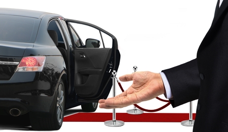 Driver standing with welcome gesture next to limousineの写真素材