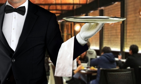 Male waiter serving in restaurant with people dining in backgroundの写真素材