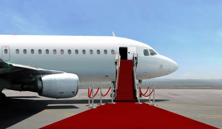 Airplane with red carpet on airport taxiway under bright blue skyの写真素材
