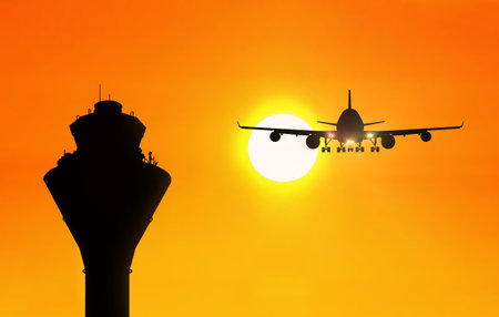 Airport traffic control tower with an airplane approaching at sunsetの写真素材