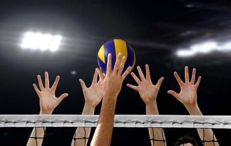 Close up of Volleyball spiking and hand blocking over the net under bright spotlightsの写真素材