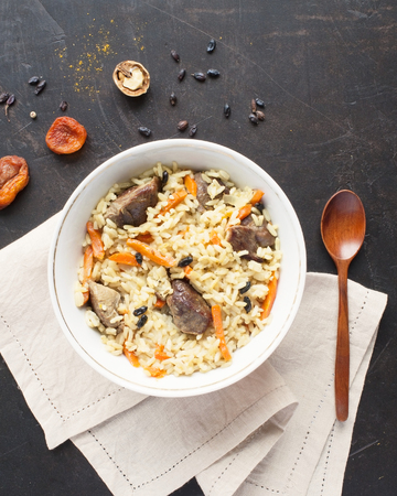 oriental dish called plov made of lamb, rice, garlic, carrots, onion and flavoured with jeera, saffron and barberry on worn brown and black backgroundの写真素材