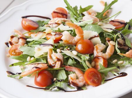 italian salad with shrimps, arugula, tomatos, parmesan cheese, pine nut, olive oil and vinegar dressing on white plate. selective focus.の写真素材