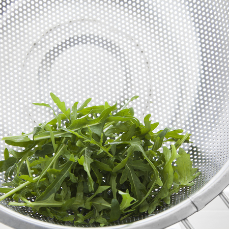 fresh green arugula leaves in metal colanderの写真素材