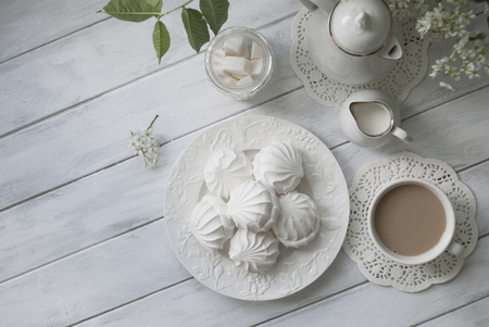 Russian marshmallow or zefir dessert on white plate with branches of blooming bird cherry tree, coffee pot, cup of coffee and milk jug on grey wooden tableの写真素材