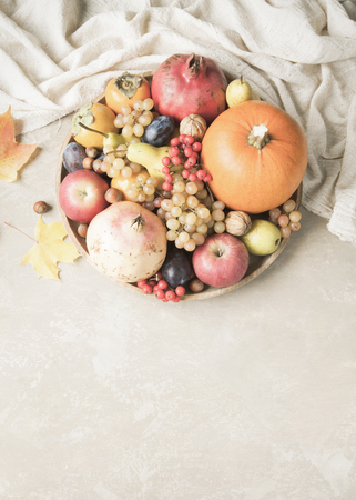 Autumn food concept. Fruits, vegetables and nuts on a wooden round tray on a light brown background.の写真素材