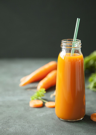 A bottle of fresh carrot juice with fresh carrots on dark background.の写真素材