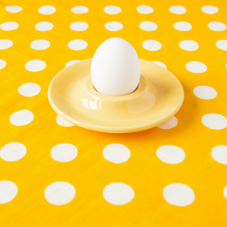 A boiled egg in an egg cup on yellow rumpled dotted cloth. Minimal.の写真素材