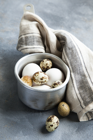 Metallic sauce pan with raw hen and quail eggs on dark shabby background.の写真素材