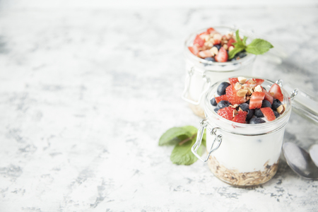 Granola with yougurt, mint and berries in jars on white and grey shabby background. Copy space.の写真素材